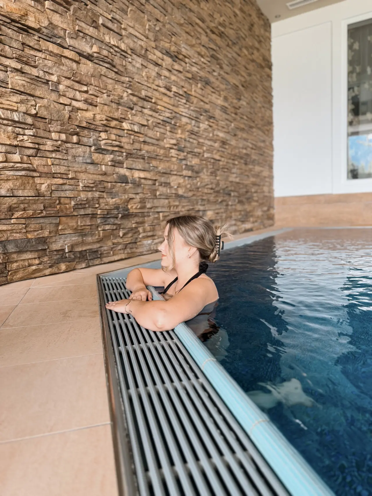 Alpinresort Schillerkopf in Bürserberg – Entspannte Frau im modernen Innenpool mit Steinwand | Wellnesshotel Vorarlberg