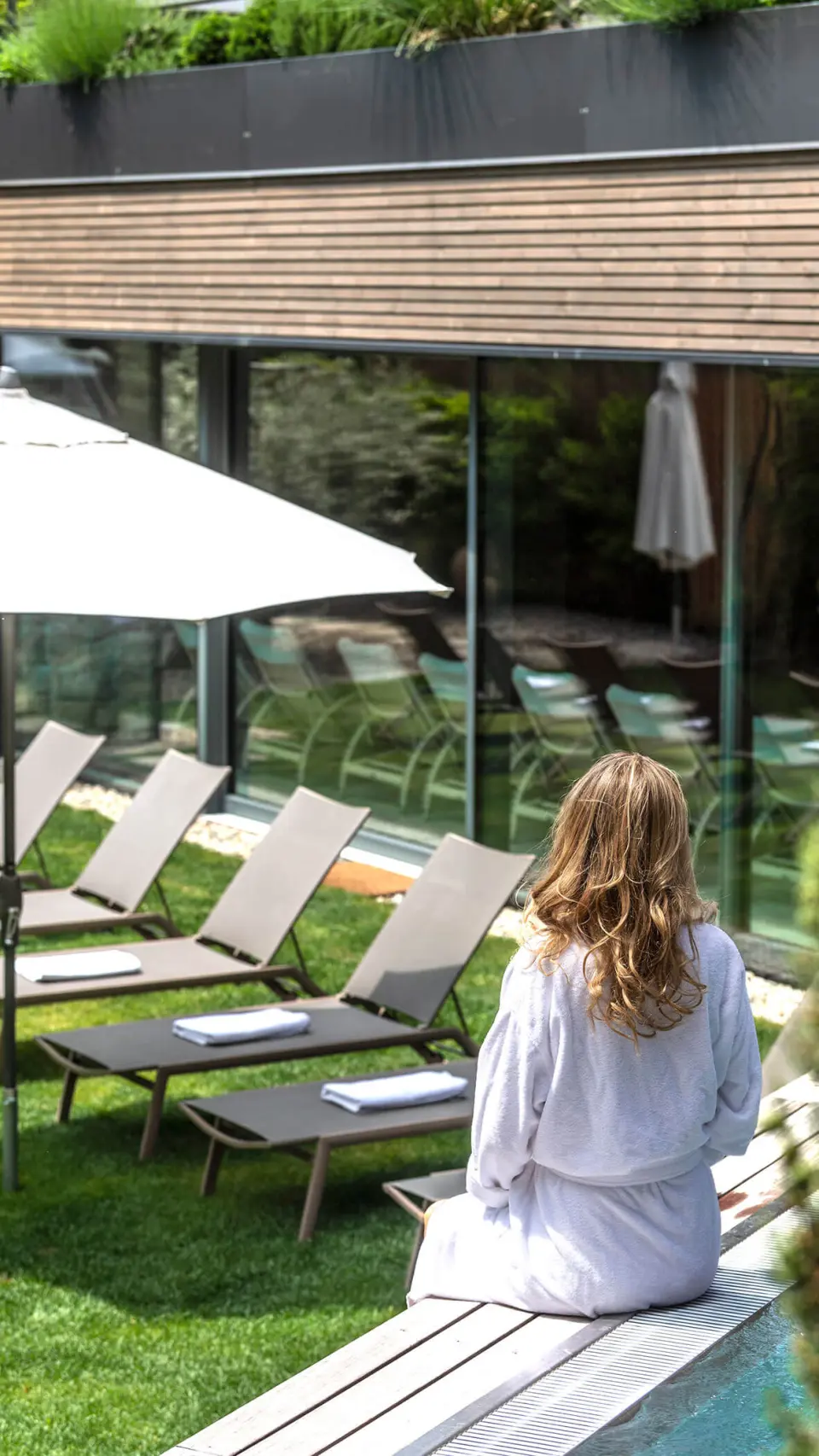 Hotel das stachelburg in Plaus – Frau im Bademantel am Außenpool mit Liegen | Wellnesshotel Südtirol