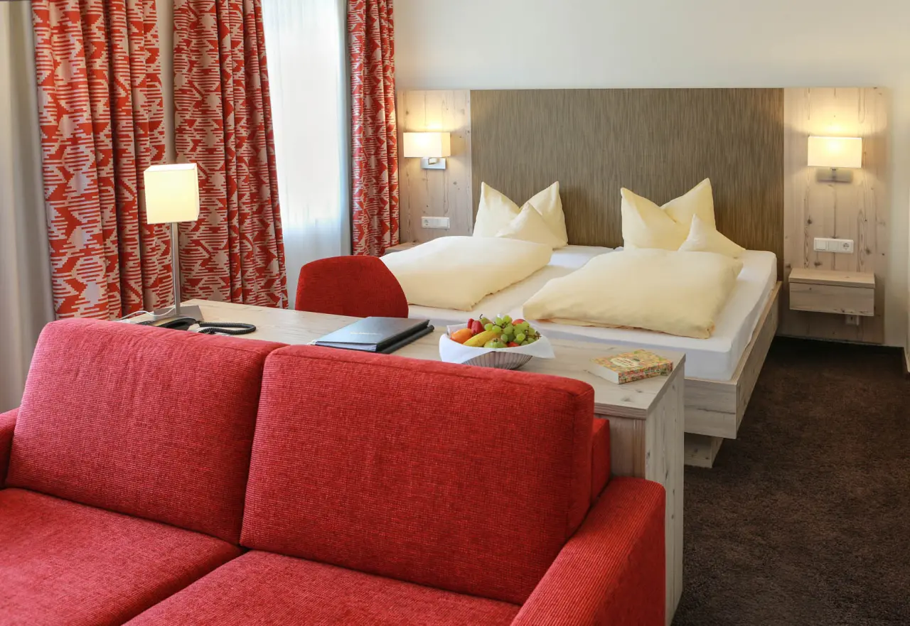 Rüters Parkhotel in Willingen – Gemütliches Zweibettzimmer mit rotem Sofa und frischem Obst | Wellnesshotel Sauerland