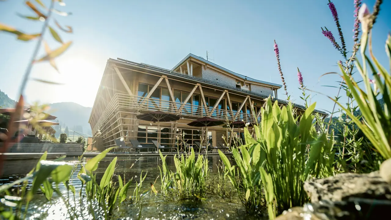 Hubertus Mountain Refugio Allgäu in Balderschwang – Moderne Hotelfassade mit Naturteich | Wellnesshotel Allgäu