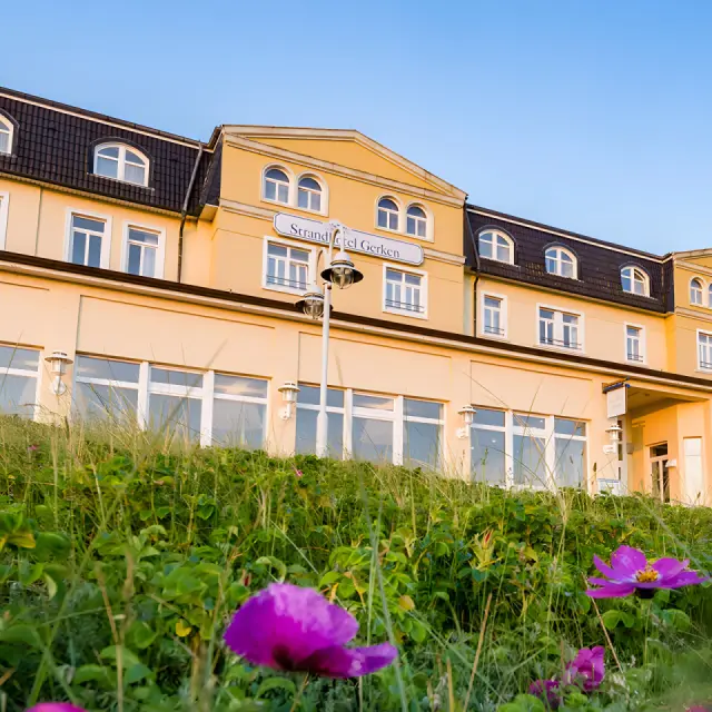 Strandhotel Gerken in Wangerooge – Hotelansicht mit blühenden Pflanzen im Vordergrund | Wellnesshotel Nordsee