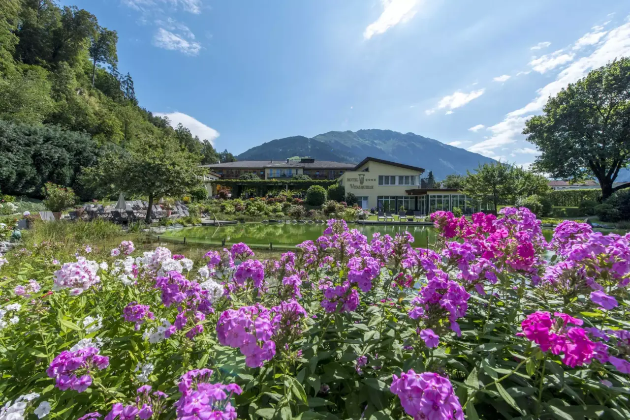 Vitalquelle Montafon in Schruns – Hotelansicht mit blühendem Garten und Naturteich | Wellnesshotel Montafon