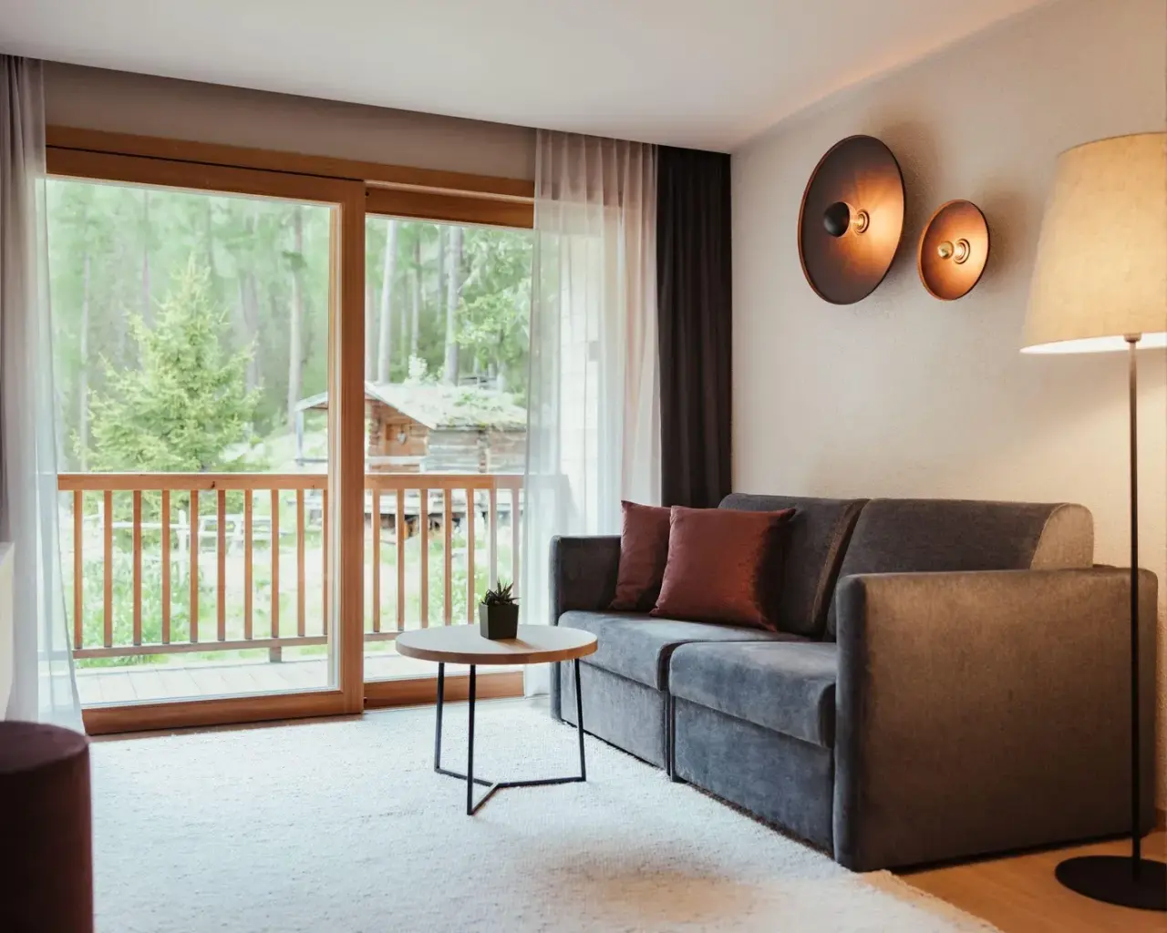 Hotel Restaurant Lëch da Sompunt in La Villa – Geräumiger Wohnbereich mit Sofa und Waldblick vom Balkon | Wellnesshotel Dolomiten