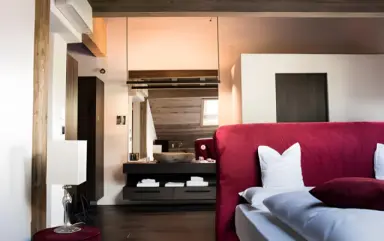 Romantik Hotel Turm in Kastelruth – Elegantes Hotelzimmer mit rotem Bett und offenem Badbereich | Wellnesshotel Südtirol