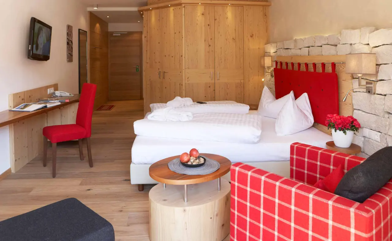 Hotel Stoeres in La Villa – Gemütliches Doppelzimmer mit Holzelementen und roten Akzenten | Wellnesshotel Dolomiten