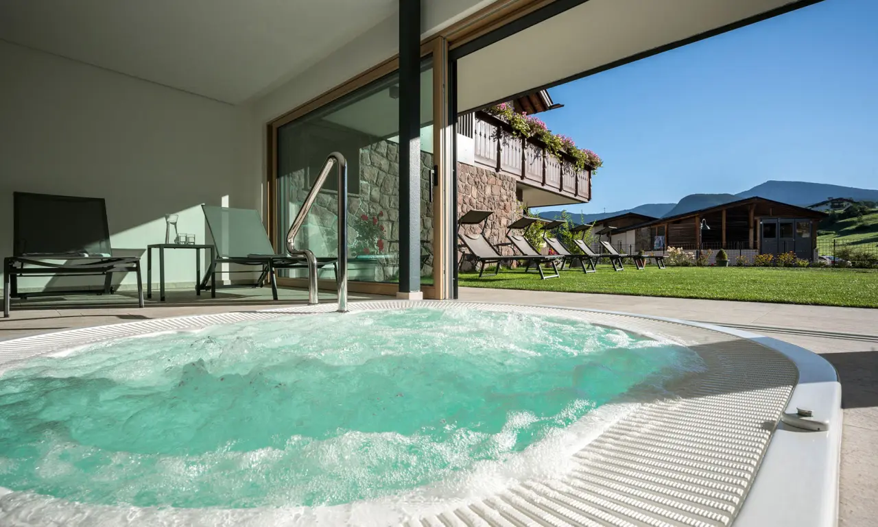 Residence Montana in Kastelruth – Außen-Whirlpool mit Blick auf die grüne Gartenanlage und Berge | Wellnesshotel Südtirol