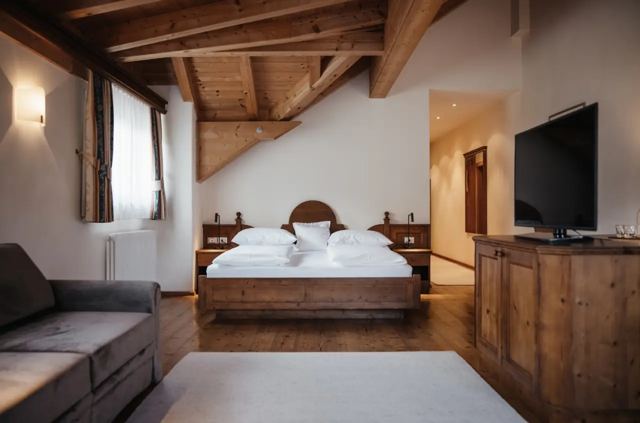 Hotel Corona in San Vigilio di Marebbe – Geräumiges Hotelzimmer mit Holzbalken und Sofa | Wellnesshotel Dolomiten