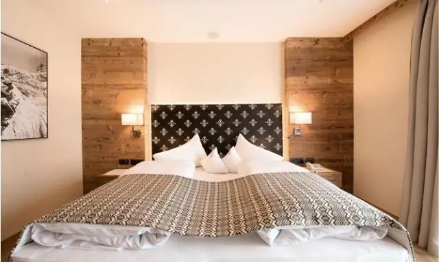 Hotel Plunhof in Ridnaun – Komfortables Doppelbett mit stilvollem Kopfteil im Hotelzimmer | Wellnesshotel Alpen