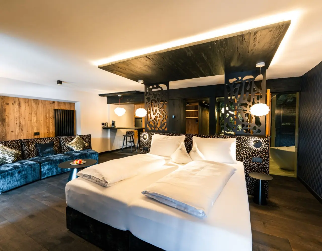 Hotel Christiania in La Villa – Elegantes Doppelzimmer mit Sofa, Bar und Badewanne im Hintergrund | Wellnesshotel Dolomiten
