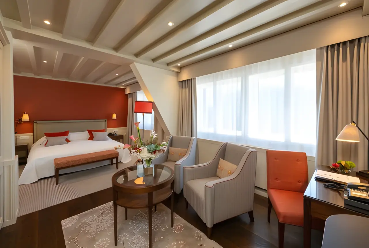 Suvretta House in St. Moritz – Komfortables Hotelzimmer mit Sitzbereich und roter Akzentwand | Wellnesshotel Engadin
