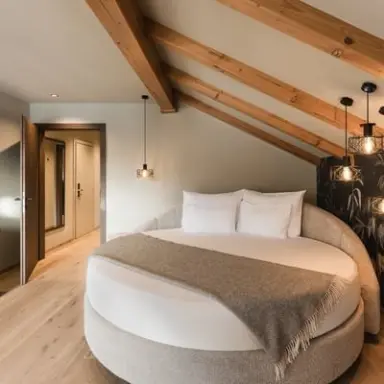 Falkensteiner Hotel Antholz in St. Martin in Gsies – Modernes Hotelzimmer mit Rundbett und Holzbalken | Wellnesshotel Südtirol